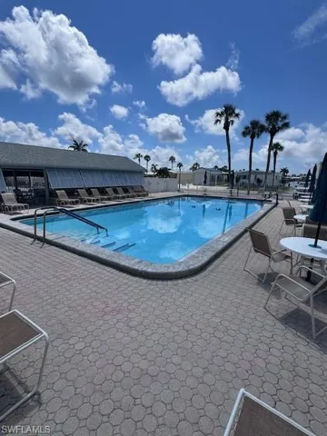 Outdoor swimming pool with integrated steps, surrounded by patterned paver decking, and an adjacent building with a gabled roof