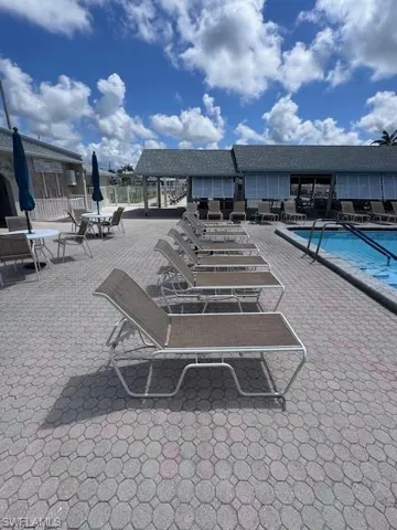 Paved pool deck with a perimeter fence and buildings featuring shuttered windows