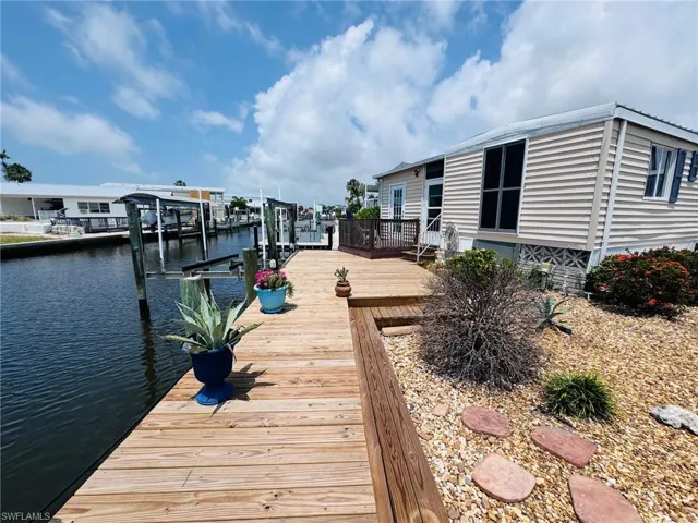 Waterfront property featuring a wooden deck, boat slips, a gravel landscape with stepping stones, and a side entry with deck access