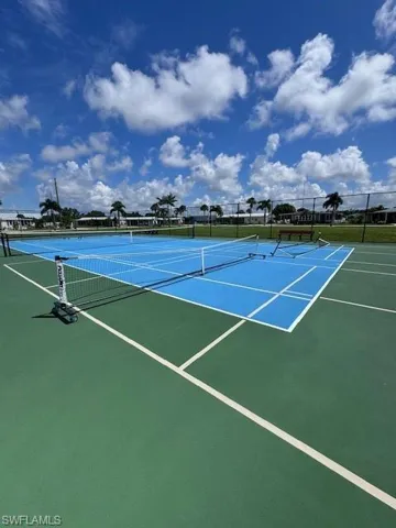 Hard tennis court surface with blue and green playing areas, surrounded by perimeter fencing