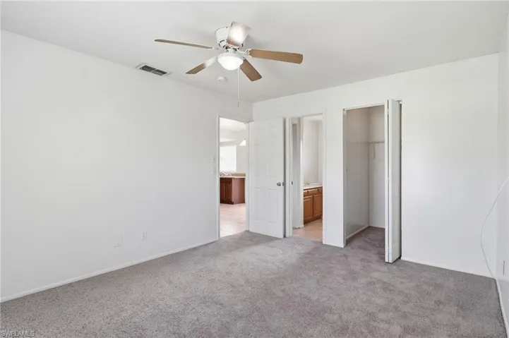 Unfurnished bedroom featuring a walk in closet, light colored carpet, and ceiling fan