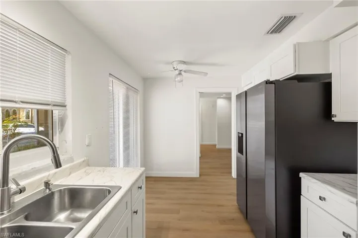 Kitchen featuring stainless steel refrigerator with ice dispenser, white cabinetry, light countertops, light wood-style flooring, and ceiling fan