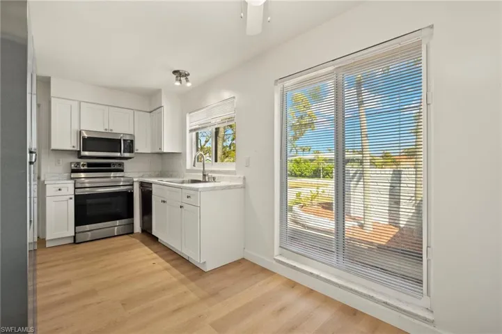 Kitchen featuring stainless steel appliances, white cabinetry, light countertops, light wood-style flooring, and a ceiling fan