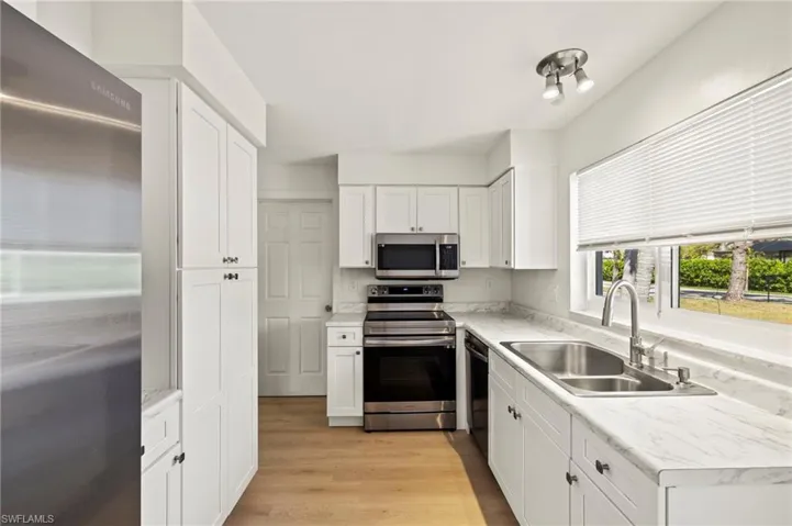 Kitchen featuring stainless steel appliances, light countertops, white cabinets, and light wood-type flooring