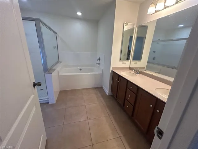 Bathroom featuring a garden tub, double vanity, light tile patterned flooring, and a stall shower