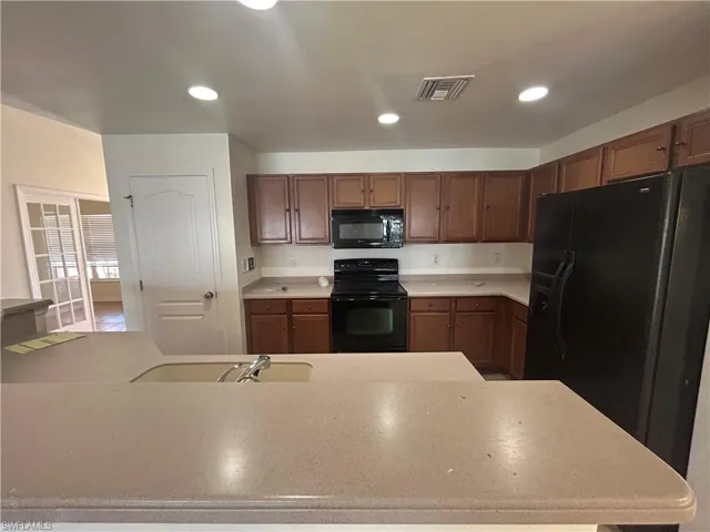 Kitchen featuring black appliances, recessed lighting, and light stone counters
