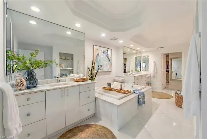 Full bathroom with recessed lighting, light tile patterned floors, a garden tub, two vanities, and a raised ceiling