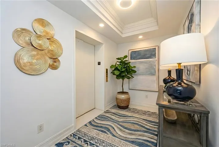 Hallway with recessed lighting, elevator, ornamental molding, and a raised ceiling