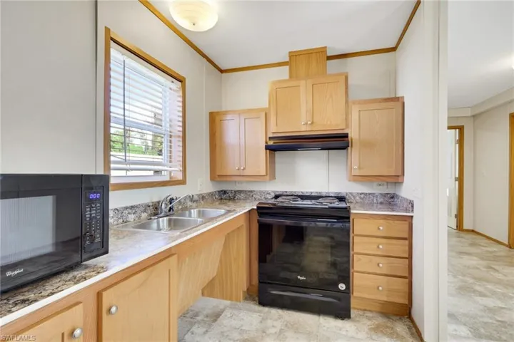 Kitchen featuring black appliances, light countertops, light brown cabinets, under cabinet range hood, and ornamental molding