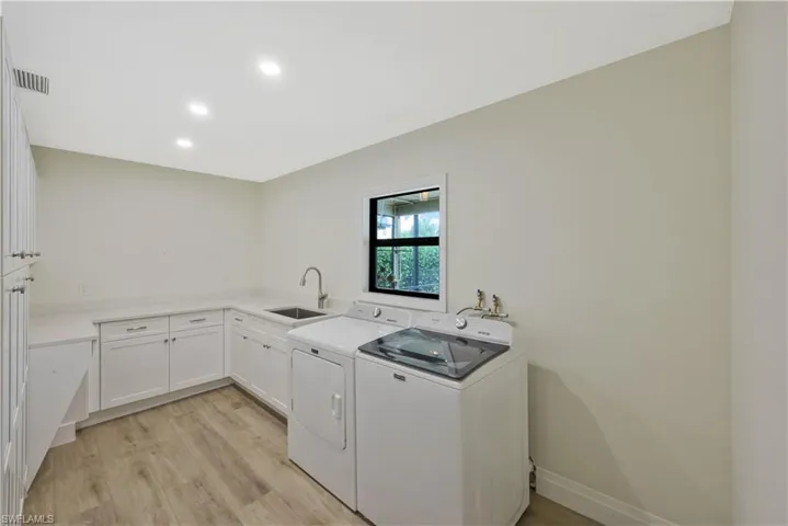 Laundry room with light wood-style floors, washer and dryer, cabinet space, and recessed lighting