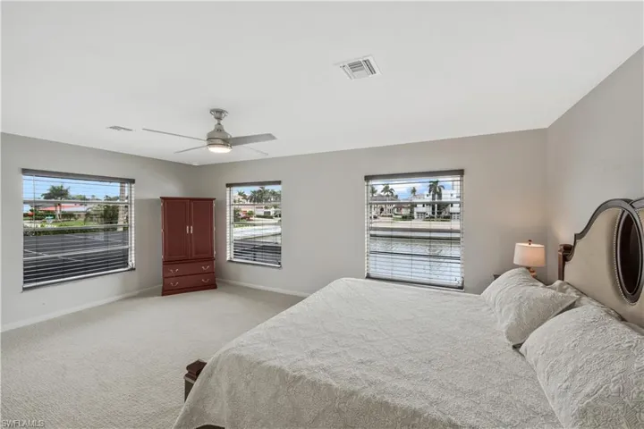 Bedroom featuring light colored carpet, multiple windows, and ceiling fan