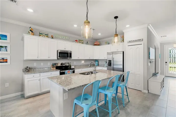 Kitchen with stainless steel appliances and finishes, sink with garbage disposal, granite countertops, and white cabinets.