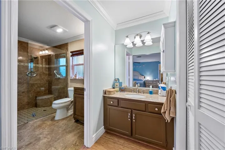 Ensuite bathroom with toilet, ensuite bathroom, vanity, a stall shower, and crown molding