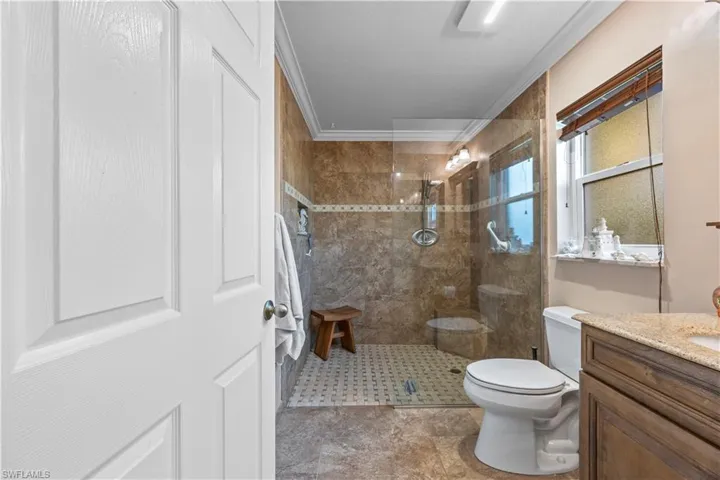 Full bath with toilet, a walk in shower, vanity, and ornamental molding