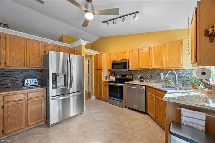 Kitchen with light stone countertops, a sink, backsplash, vaulted ceiling, and appliances with stainless steel finishes