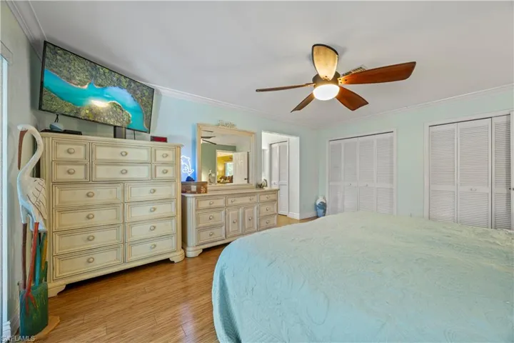 Bedroom featuring light wood-type flooring, ornamental molding, ceiling fan, and multiple closets