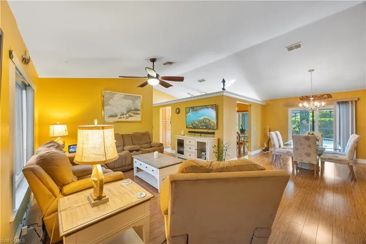 Living area with visible vents, wood finished floors, lofted ceiling, and ceiling fan with notable chandelier