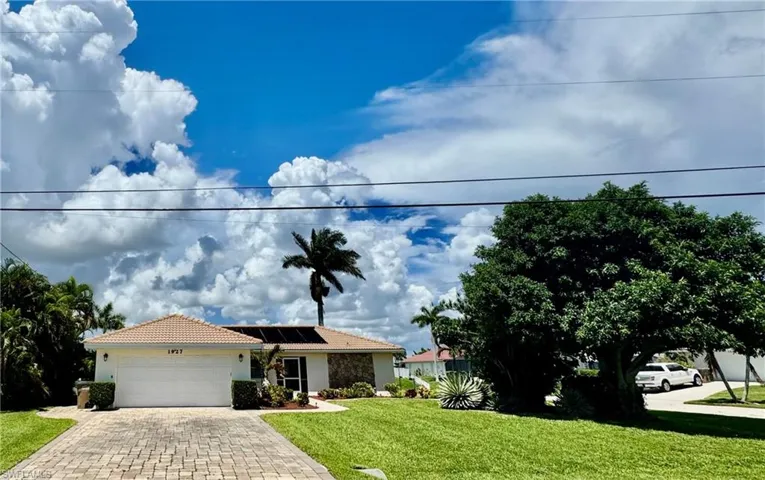 Single story home featuring solar panels, an attached garage, a front lawn, decorative driveway, and stucco siding