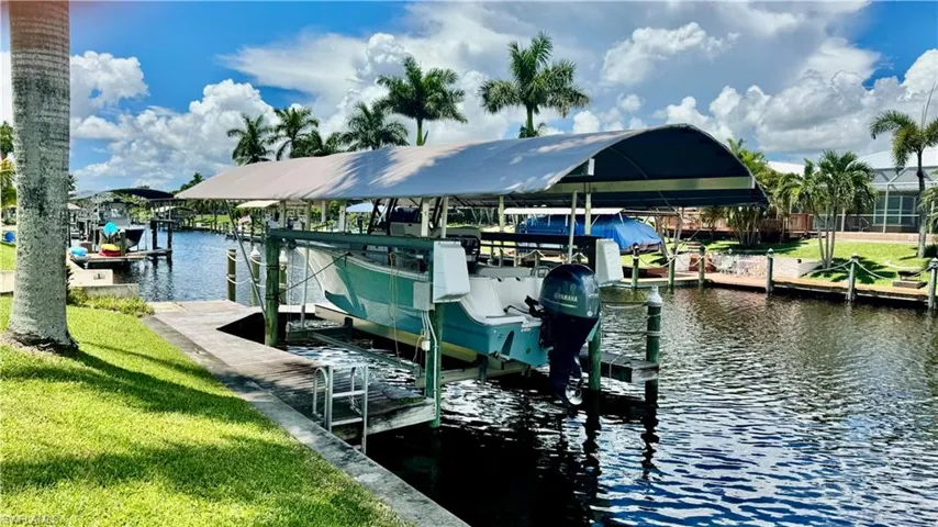 Dock featuring boat lift, a water view, and a yard