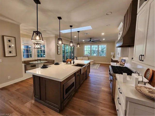 Kitchen with dual tone cabinets, dark wood-style flooring, a skylight, a ceiling fan, and a kitchen island with sink