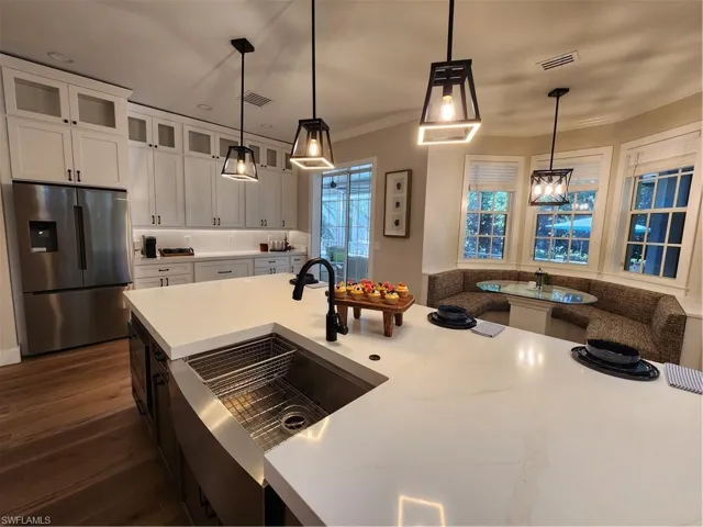 Two tone kitchen featuring glass fronted cabinets, fridge, dark wood-style floors, two tone cabinetry, and hanging light fixtures