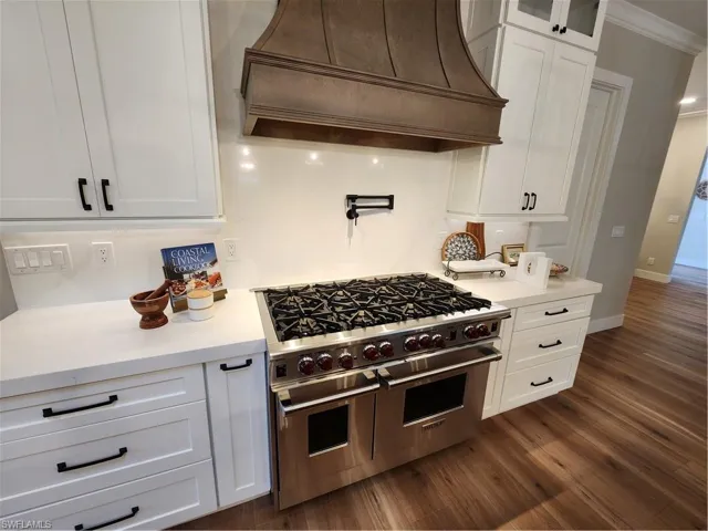 Kitchen with stove, ventilation hood, white cabinets, ornamental molding, and glass fronted cabinets
