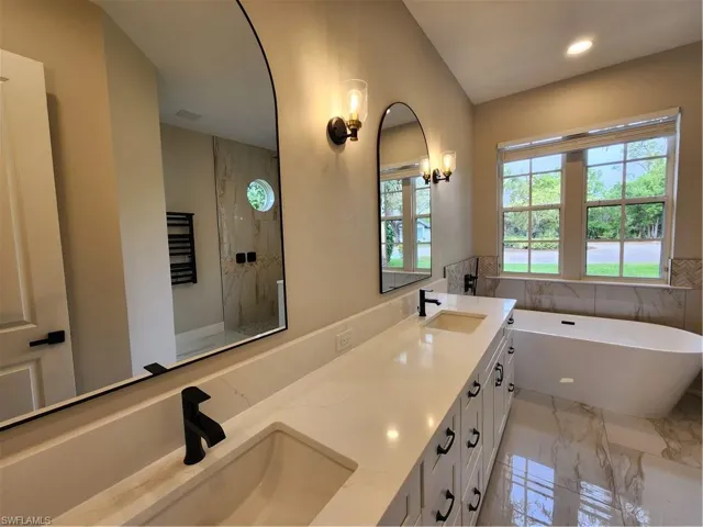 Full bath featuring light marble finish floors, double vanity, a freestanding bath, recessed lighting, and a marble finish shower