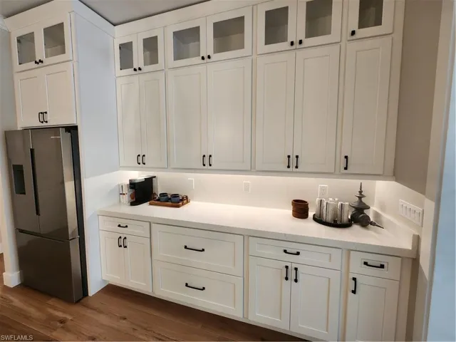 Kitchen with stainless steel refrigerator, glass fronted cabinets, white cabinetry, and light stone counters