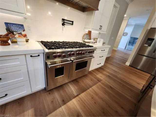 Kitchen featuring white cabinetry, range with two ovens, refrigerator, dark wood-style flooring, and ornamental molding