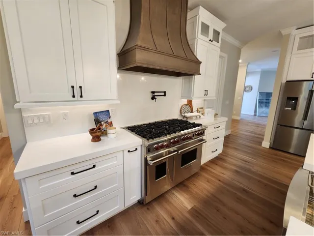 Kitchen with white cabinetry, freestanding refrigerator, stove, ornamental molding, and range hood
