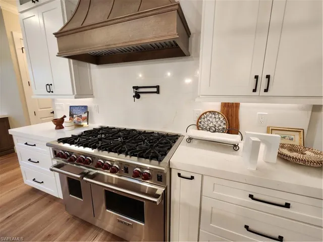 Kitchen with range, extractor fan, white cabinetry, light stone counters, and light wood-style floors