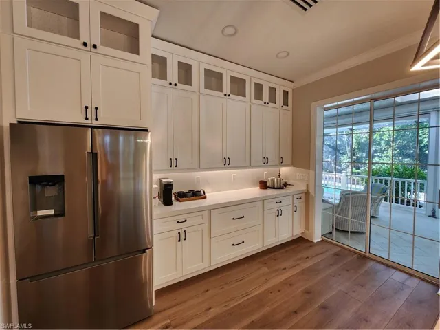 Kitchen featuring refrigerator, glass fronted cabinets, white cabinets, dark wood-style flooring, and crown molding