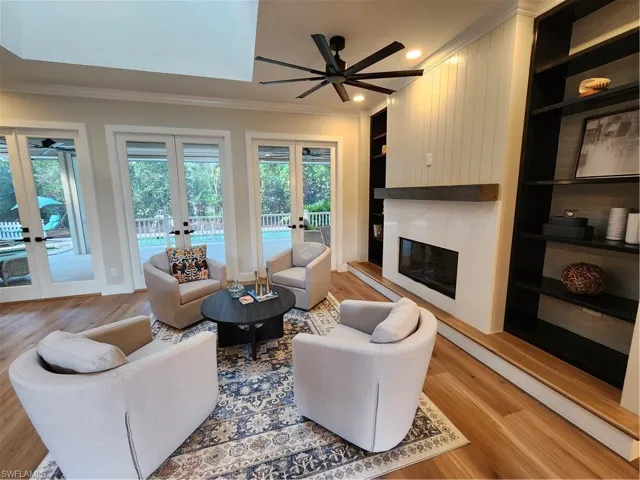 Living room with built in shelves, ceiling fan, french doors, crown molding, and light wood-style floors
