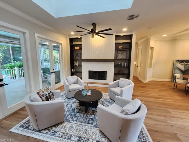 Living area with crown molding, light wood-style floors, a premium fireplace, built in shelves, and a ceiling fan