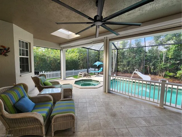 View of patio with an in-ground hot tub, glass enclosure, ceiling fan, and view of scattered trees