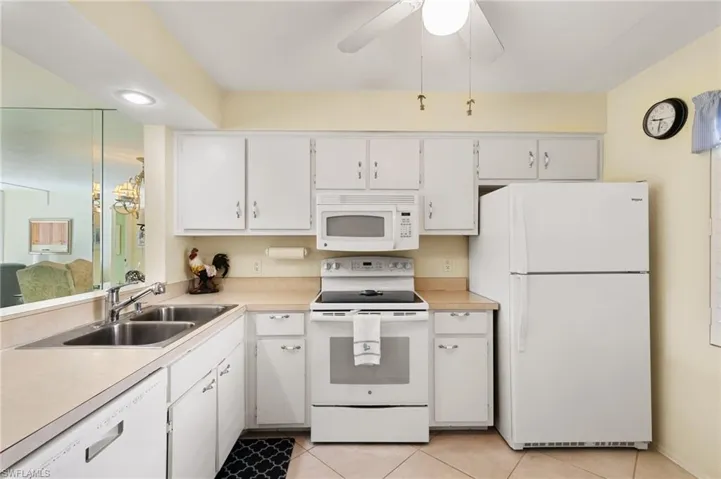 Kitchen featuring white cabinetry, sink, white appliances, ceiling fan, and light tile patterned flooring