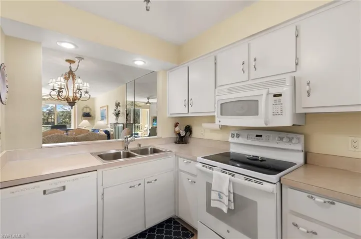 Kitchen with white appliances, white cabinets, decorative light fixtures, a chandelier, and sink