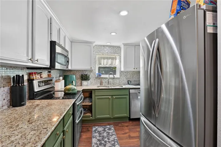 Kitchen featuring stainless steel appliances, dual tone cabinets, light stone countertops, dark wood-style floors, and recessed lighting