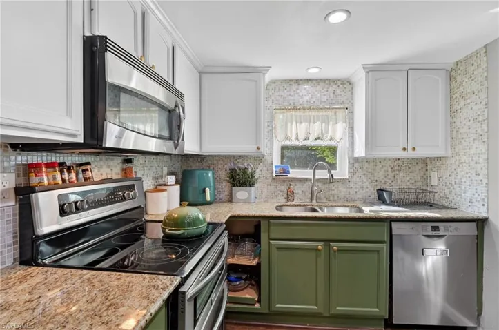 Dual tone kitchen featuring stainless steel appliances, two tone color scheme, light stone counters, and decorative backsplash
