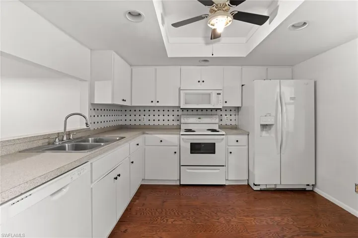 Kitchen featuring white appliances, dark wood finished floors, white cabinetry, decorative backsplash, and recessed lighting