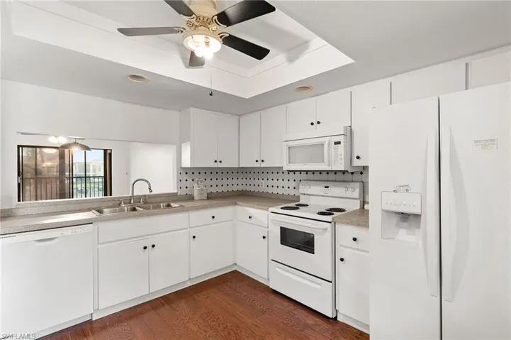 Kitchen featuring white appliances, a raised ceiling, white cabinetry, and dark wood-type flooring