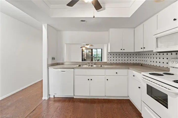 Kitchen with white appliances, white cabinetry, dark wood-style flooring, and ceiling fan