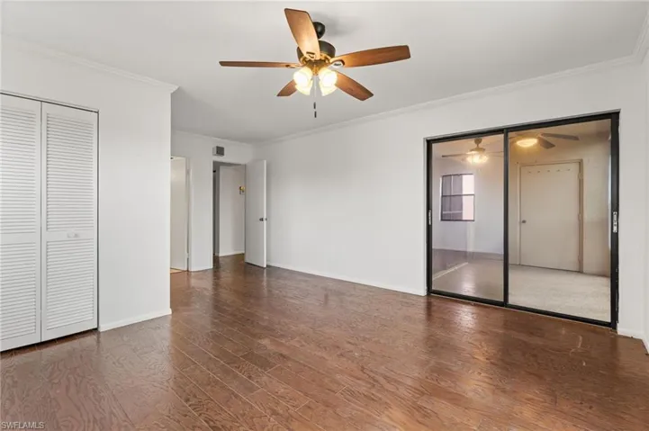 Unfurnished bedroom with ornamental molding, dark wood-style floors, a ceiling fan, and two closets