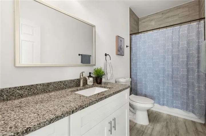 Bathroom with toilet, vanity, shower / tub combo with curtain, and wood finished floors