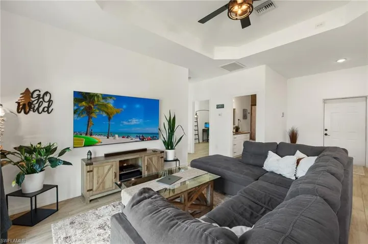 Living area featuring light wood-style flooring, a ceiling fan, a raised ceiling, and visible vents