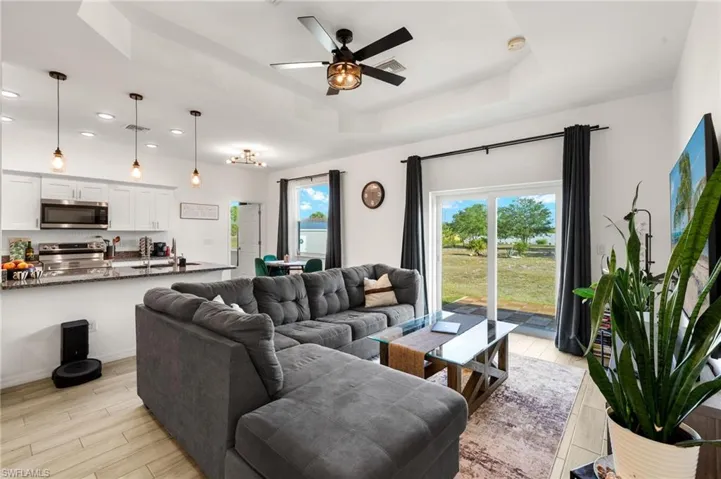 Living area featuring a tray ceiling, a ceiling fan, light wood-style flooring, visible vents, and recessed lighting