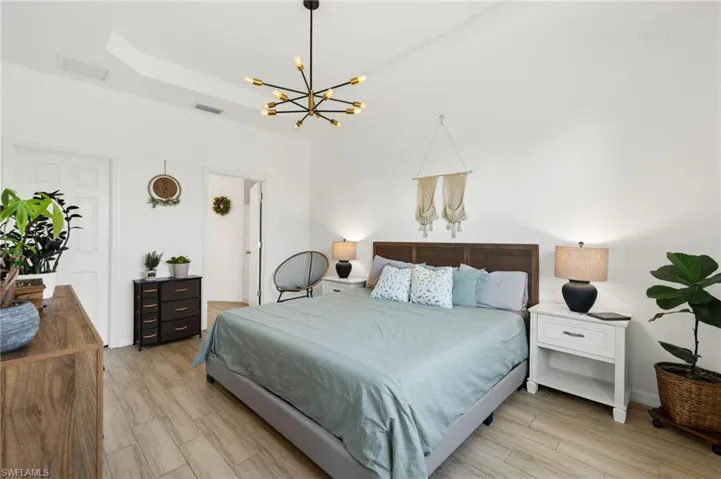 Bedroom featuring visible vents, light wood-type flooring, a notable chandelier, and a raised ceiling