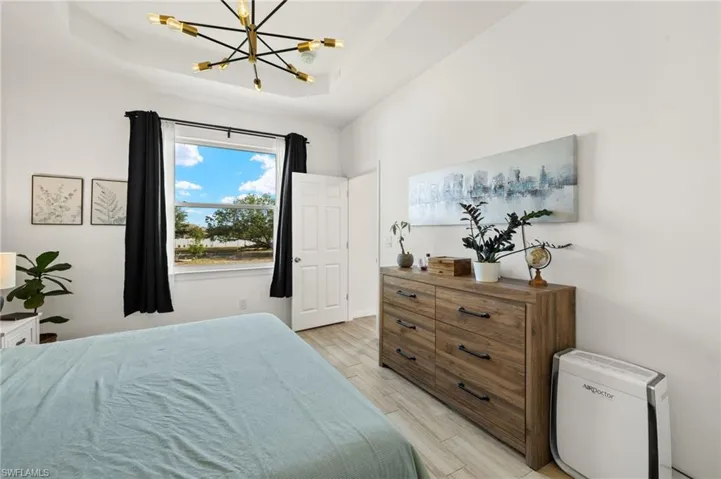 Bedroom featuring light wood finished floors, a notable chandelier, and a raised ceiling