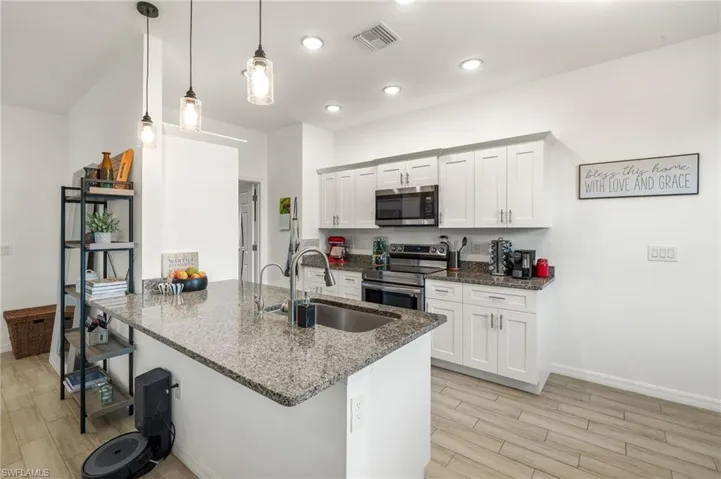Kitchen with wood finish floors, dark stone countertops, a breakfast bar, a sink, and appliances with stainless steel finishes