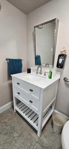 White vanity with a built-in sink and stone-finish countertop, brushed nickel faucet, and a wall-mounted rectangular mirror
